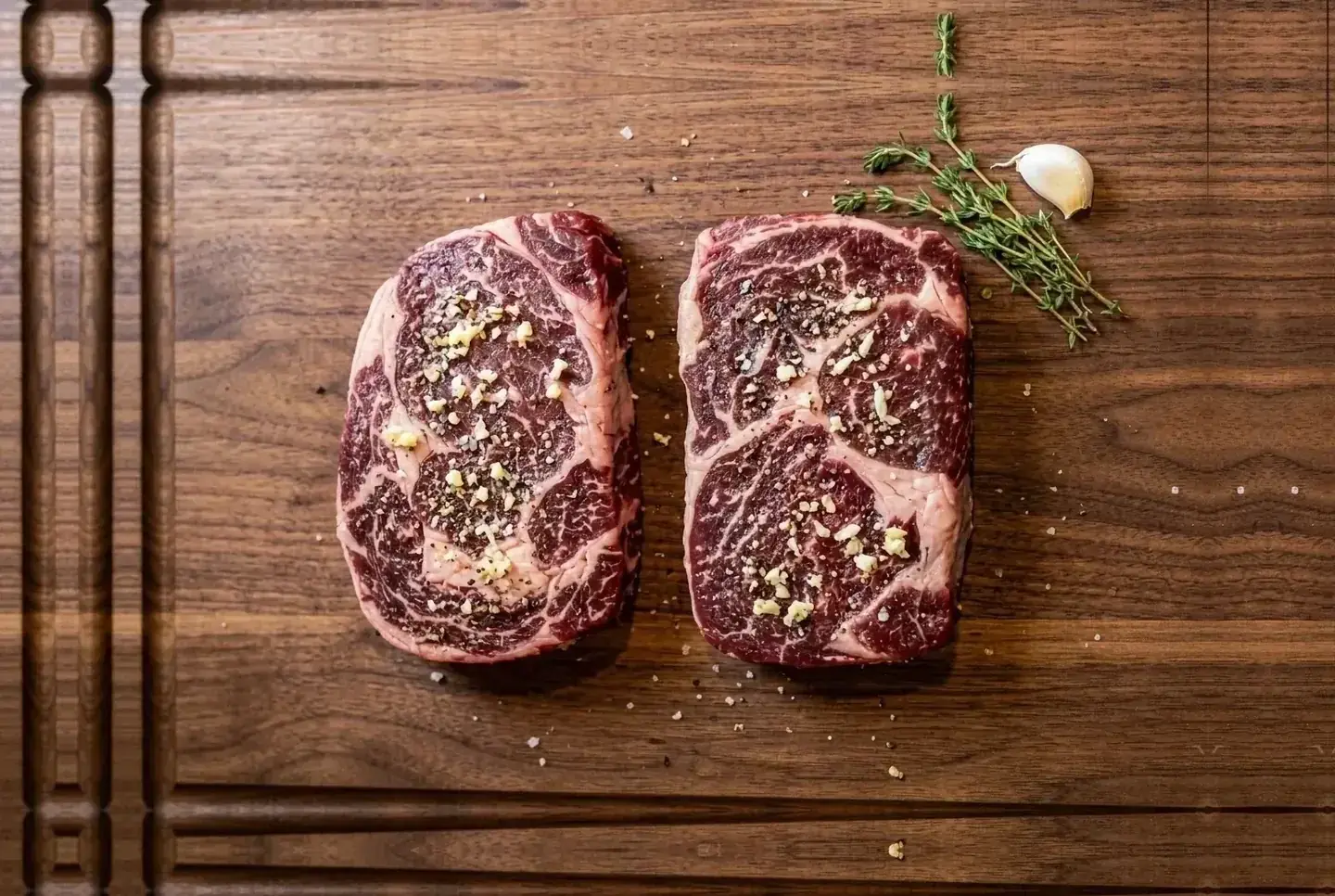 Two salted ribeyes resting on a cutting board